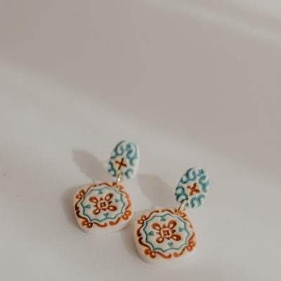 Brincos cerâmicos decorados com padrões florais azuis e castanhos sobre fundo branco