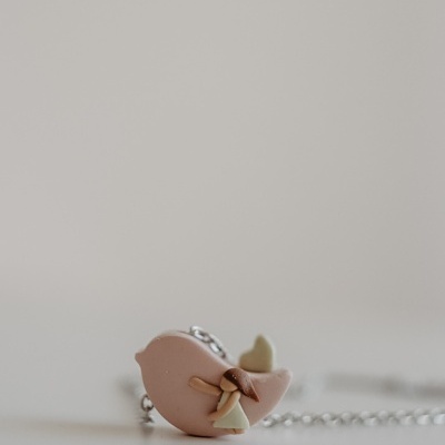 Colar com pendente rosa em forma de pássaro e rapariga abraçando-o.
