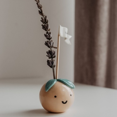 Vaso cerâmico pêssego com folhas verdes, rosto sorridente, ramo seco e bandeira branca
