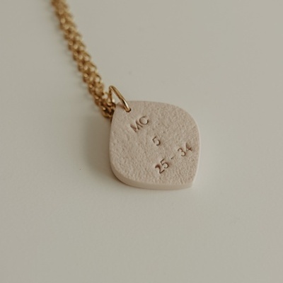 Colar com pendente bege texturizado com gravação e corrente dourada
