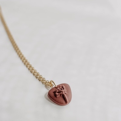 Colar dourado com coração castanho em fundo claro