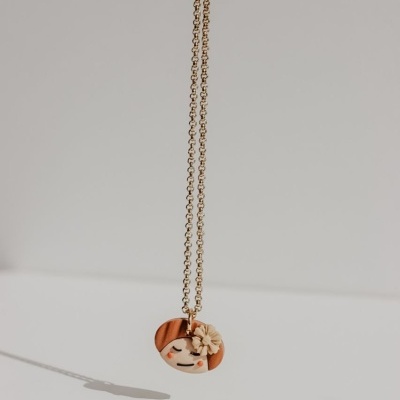 Colar dourado com pendente redondo de rosto sorridente e flor