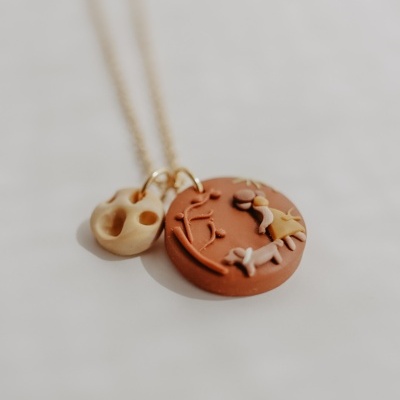 Colar dourado com pendentes de argila castanho e creme em relevo, um redondo com figuras e outro orgânico com buracos