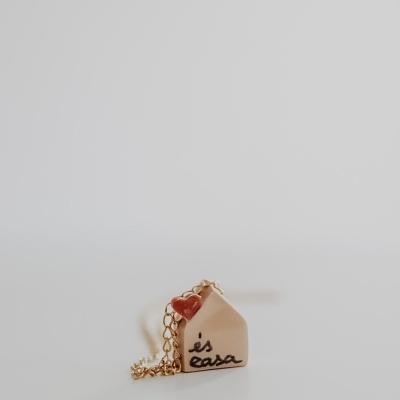 Colar com pendente de casa bege e coração vermelho em fundo branco