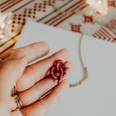 Colar com pendente vermelho com pintas brancas segurado em mão sobre fundo tecido tradicional