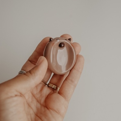 Figura de cerâmica pequena em forma de cabeça de urso castanho e bege na mão