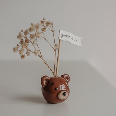 Vaso de cerâmica em forma de cabeça de urso com flores secas e bandeira branca