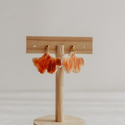Brincos em forma de folha laranja e bege pendurados num suporte de madeira