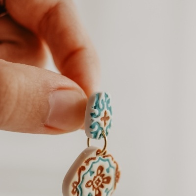 Brinco pendente de cerâmica azul e castanho segurado por uma mão