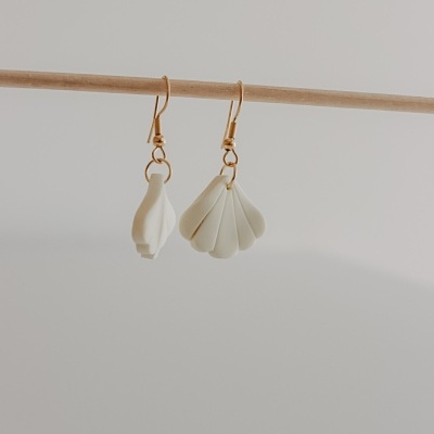 Brincos assimétricos em branco creme com argolas douradas pendurados em barra de madeira