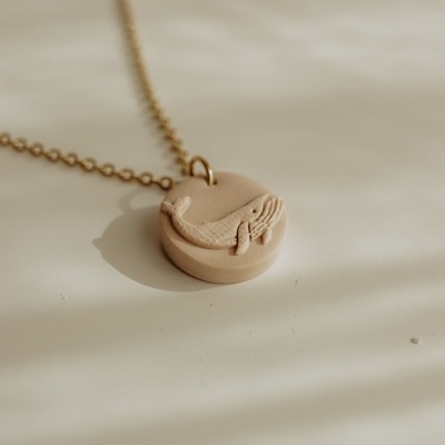 Colar dourado com pendente redondo bege com relevo de baleia