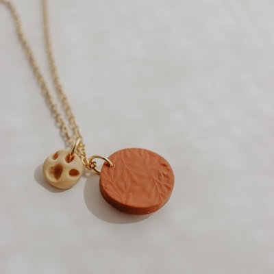 Colar dourado com dois pendentes, um terracota texturizado e outro creme com furos redondos