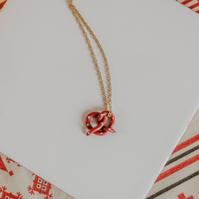 Colar com pendente de pretzel vermelho com pontos brancos sobre superfície branca