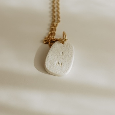 Colar dourado com pendente branco texturizado e números gravados