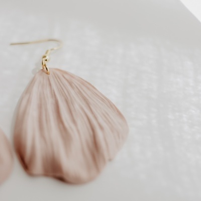 Brinco pendente bege com textura semelhante a uma pétala, com gancho dourado