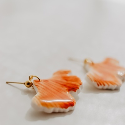 Brincos de resina laranja e branca com padrão marmoreado e fecho dourado sobre superfície branca