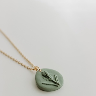 Colar dourado com pendente verde redondo e relevo de planta