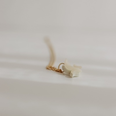 Colar dourado com pendente branco em forma de cruz sobre fundo branco