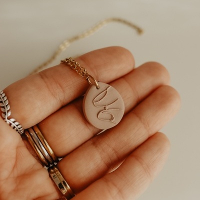 Colar com pendente redondo rosa claro e gravação abstrata na mão.