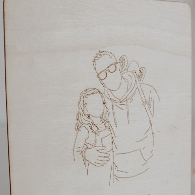 Placa de madeira clara com gravação de desenho de pai e filha e texto em português.