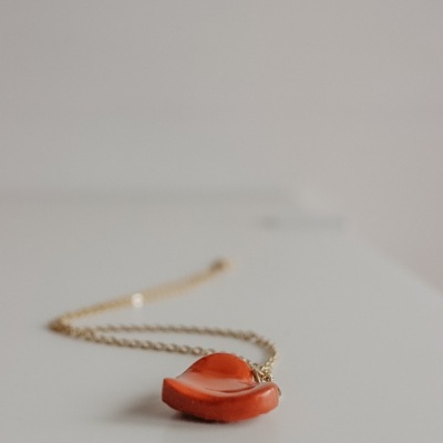 Colar dourado com pendente em forma de chapéu vermelho sobre superfície branca.