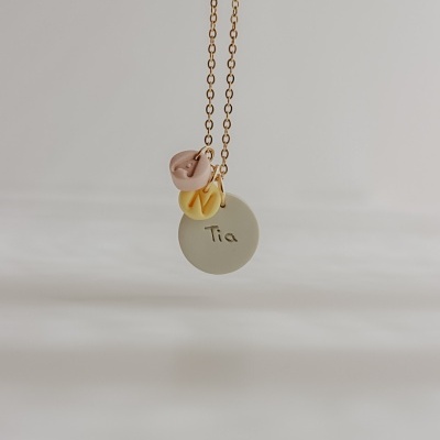 Colar dourado com três pendentes coloridos em fundo neutro