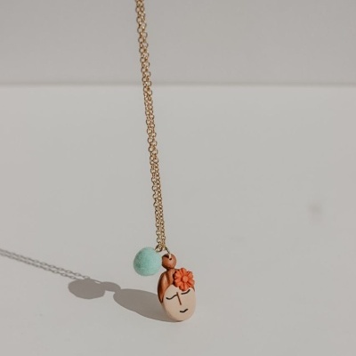 Colar dourado com pendente de rosto feminino em cerâmica e flor laranja