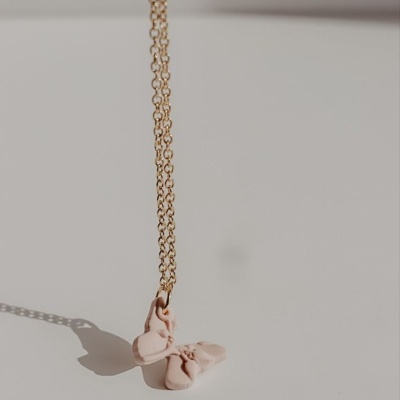 Colar dourado com pendente de laço cor de rosa claro sobre superfície branca