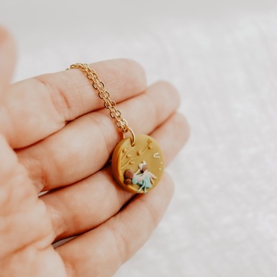 Colar com pendente redondo castanho claro com decoração colorida em relevo numa mão