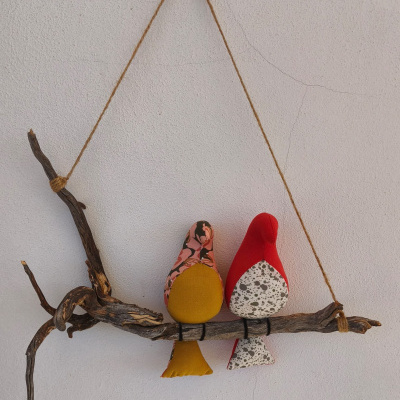 Duas figuras de pássaros em tecido penduradas num galho seco numa parede