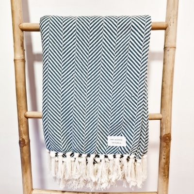 Manta azul e branca com padrão espinha de peixe pendurada numa estrutura de madeira.