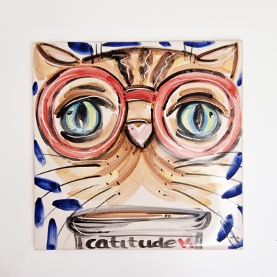 Azulejo decorativo com ilustração de gato usando óculos vermelhos grandes e texto 'catitude'.