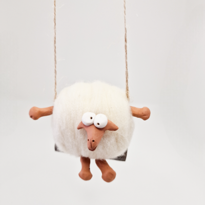 Boneco de ovelha em lã branca com cabeça e patas cor de terracota num balanço suspenso por cordas