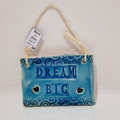 Placa decorativa azul em cerâmica com texto 'DREAM BIG' e corações pretos pendurada por cordão
