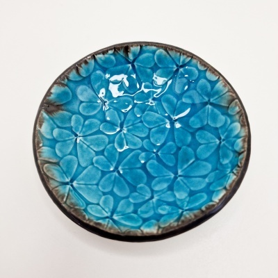 Prato redondo azul turquesa com padrão floral em relevo e bordas castanhas