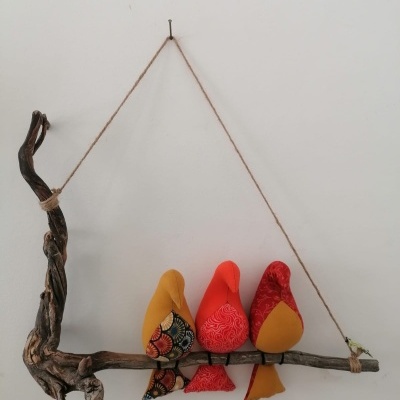 Decoração de parede com três pássaros de tecido colorido num ramo de madeira pendurado por corda