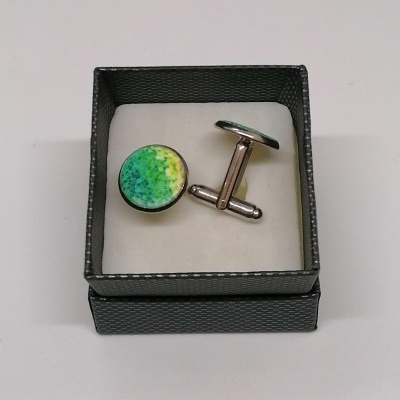 Botões de punho redondos verde amarela numa caixa preta.