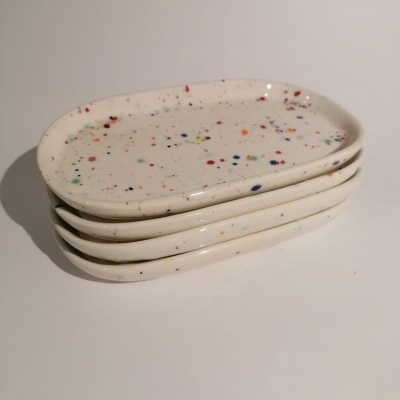 Quatro pratos ovais brancos com respingos coloridos empilhados
