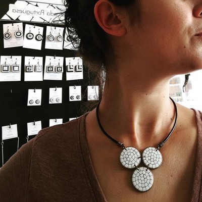 Colar com três pendentes redondos brancos com padrão de rachadura em pescoço de pessoa com fundo de brincos