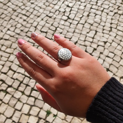 Mão com anel redondo branco com padrão preto junto a calçada portuguesa