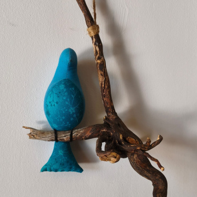 Pássaro azul de tecido com padrão floral em madeira rústica pendurado na parede.