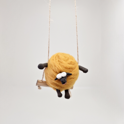 Boneco de carneiro de lã amarela sentado num baloiço de madeira