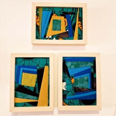 Três quadros com tecidos coloridos em padrões geométricos em molduras claras pendurados numa parede branca