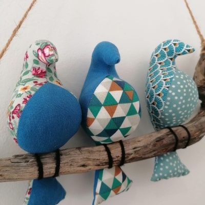 Pássaros decorativos de tecido com padrões variados pendurados num ramo de madeira
