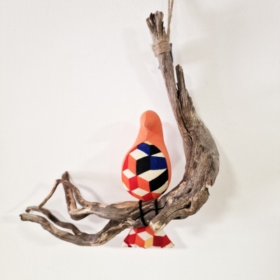 Pássaro decorativo de tecido com padrão geométrico pendurado numa peça de madeira natural.