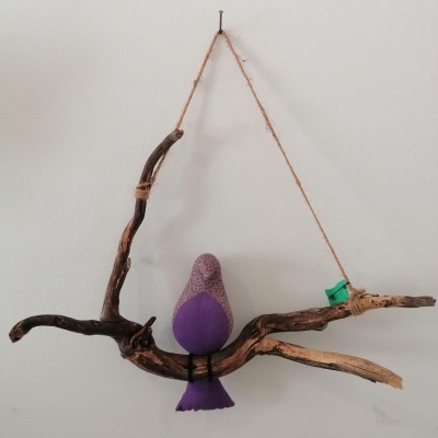 Escultura de pássaro roxo em galho de madeira pendurado na parede