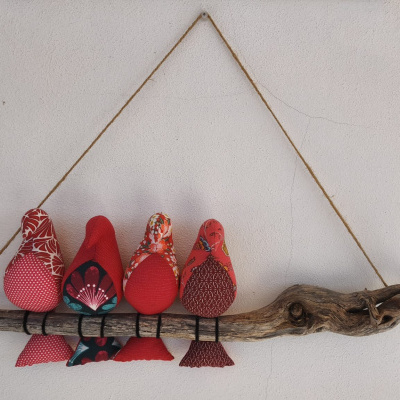 Decoração artesanal de parede com pássaros de tecido vermelhos presos a um pedaço de madeira.