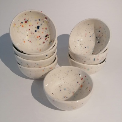 Conjunto de tigelas cerâmicas brancas com manchas coloridas, empilhadas sobre fundo branco