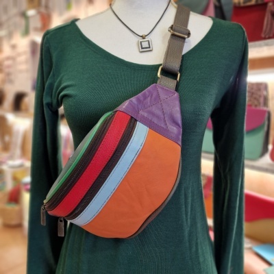 Bolsa colorida tipo pochete em alça castanha, com várias faixas de cores, sobre manequim com camisola verde escuro e colar.