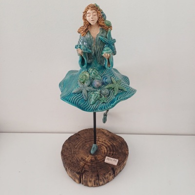 Escultura de mulher com vestido azul e elementos marinhos sobre base de madeira